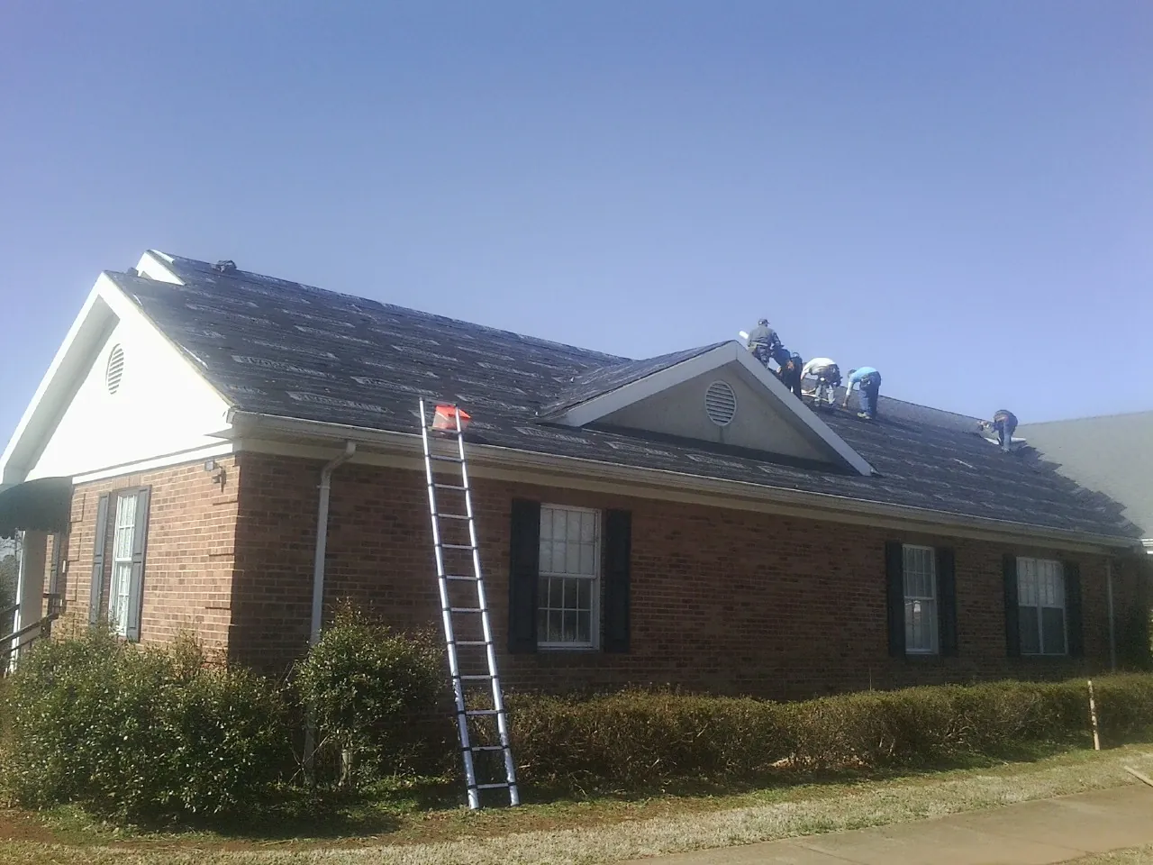 Crew tearing shingles off a brick ranch roof with a ladder set — Emergency Roof Repair work by our crew in Keokuk