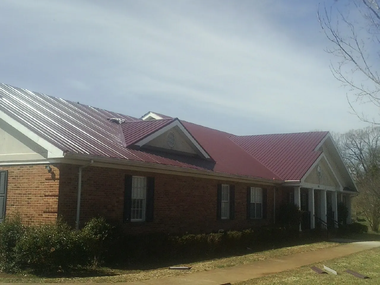 Red metal roof with gabled entries on a long brick building, from a Hail Damage Roof Repair job in Keokuk