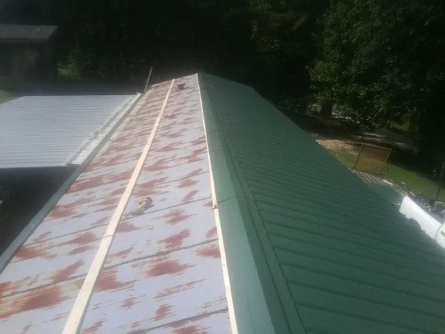 Old rusted panels beside newly installed green metal roofing — Wind Damage Roof Repair by Roofing Brothers in Keokuk