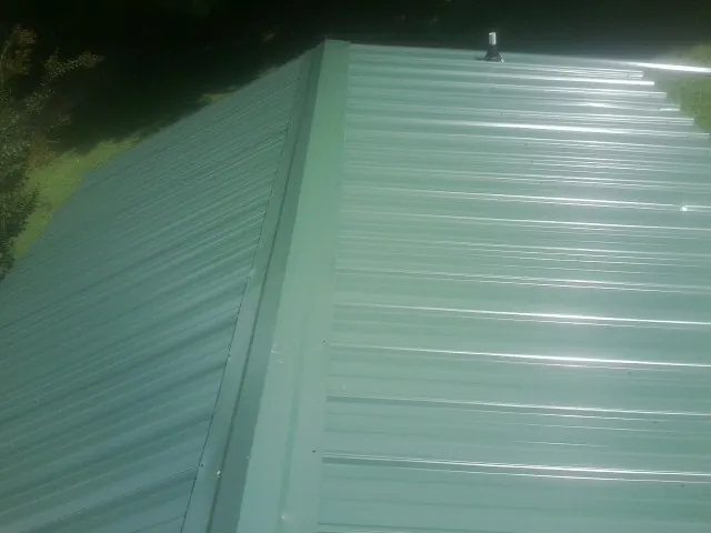New green metal panels meeting at the ridge of a roof — Flat Roof Repair work by our crew in Keokuk