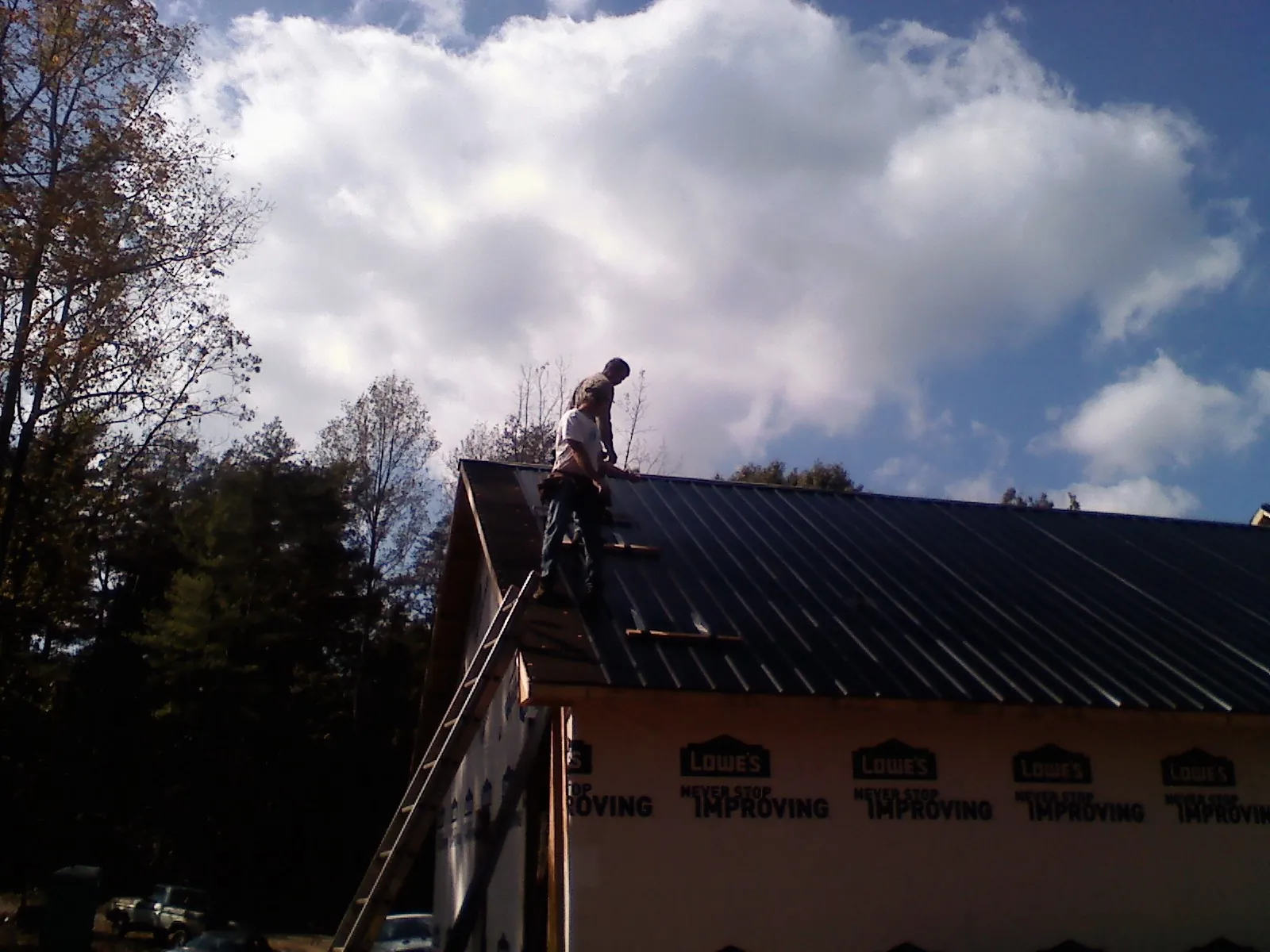 Roofer fastening dark metal panels high against a cloudy sky, from a Roof Inspection job in Keokuk