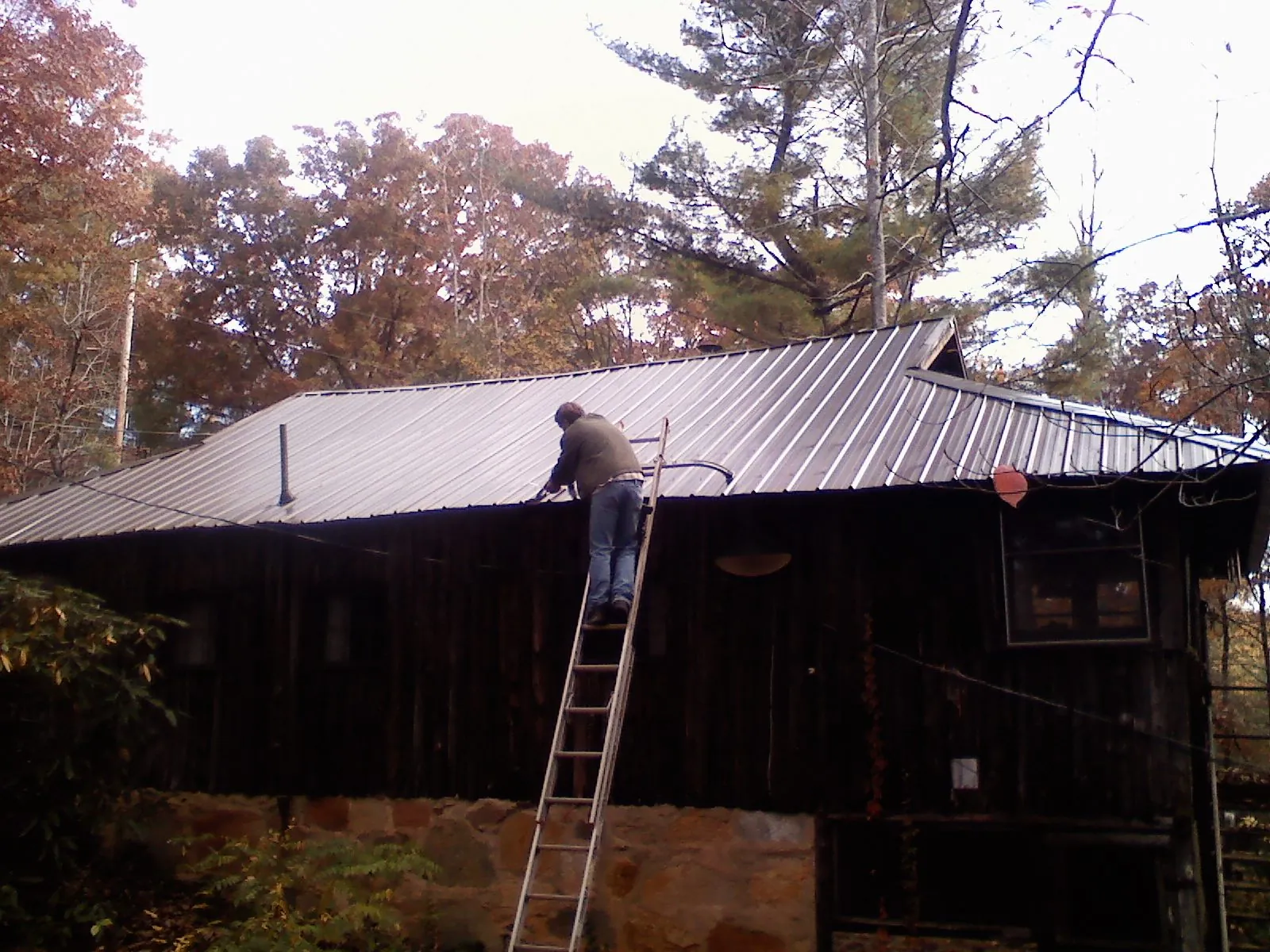 Roofer on a ladder working along the edge of a cabin metal roof in Keokuk