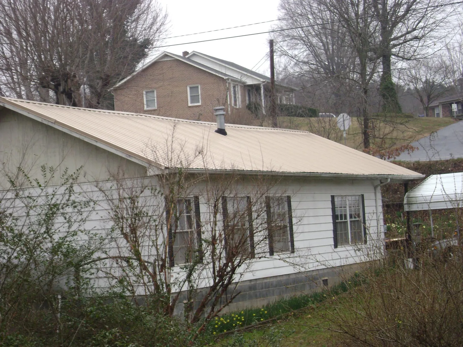 Tan metal roof on a white sided house set into a hillside — Commercial Roofing by Roofing Brothers in Keokuk