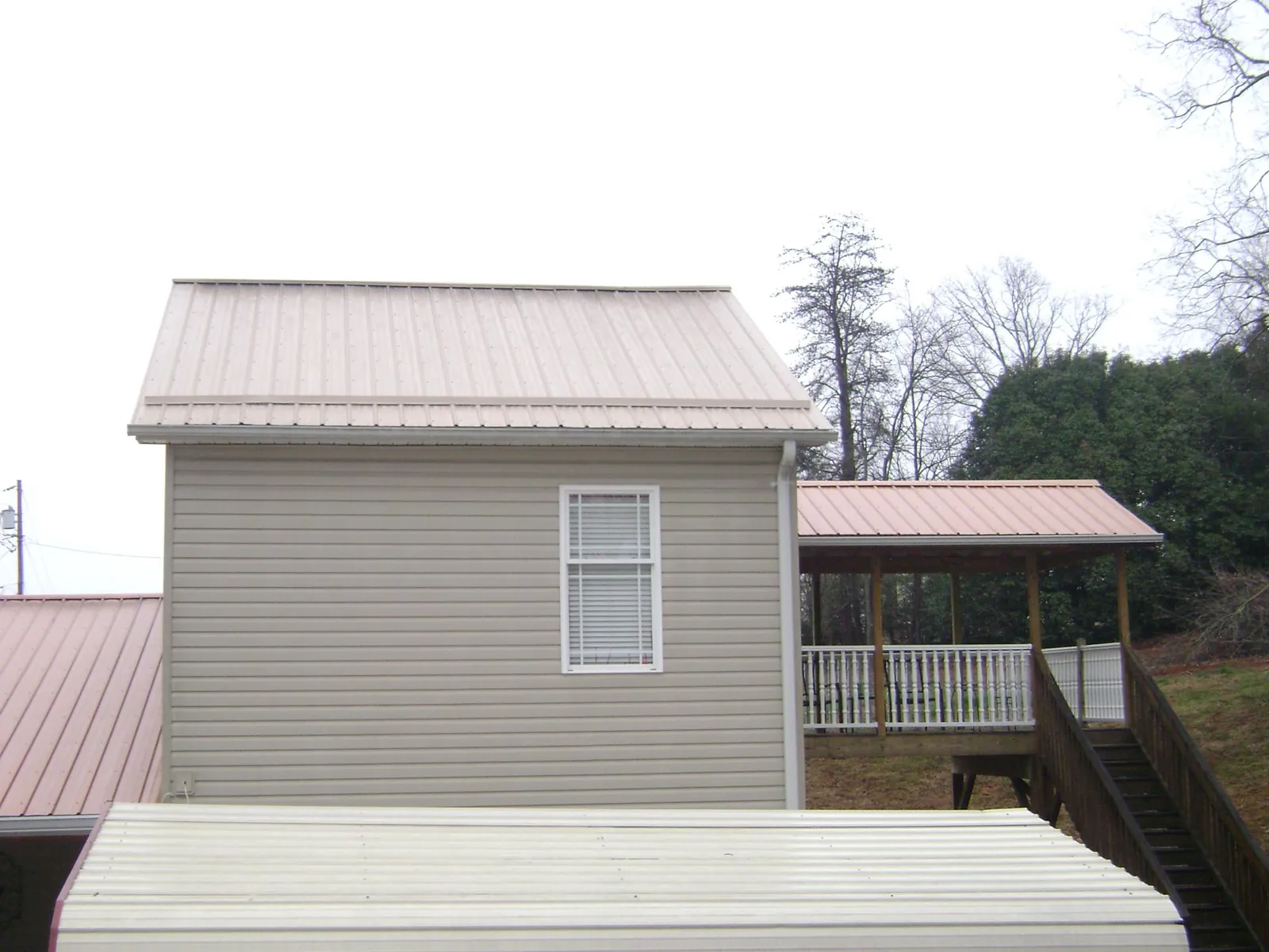 Tan metal roofs on a two story addition and attached porch, from a Roof Replacement job in Keokuk